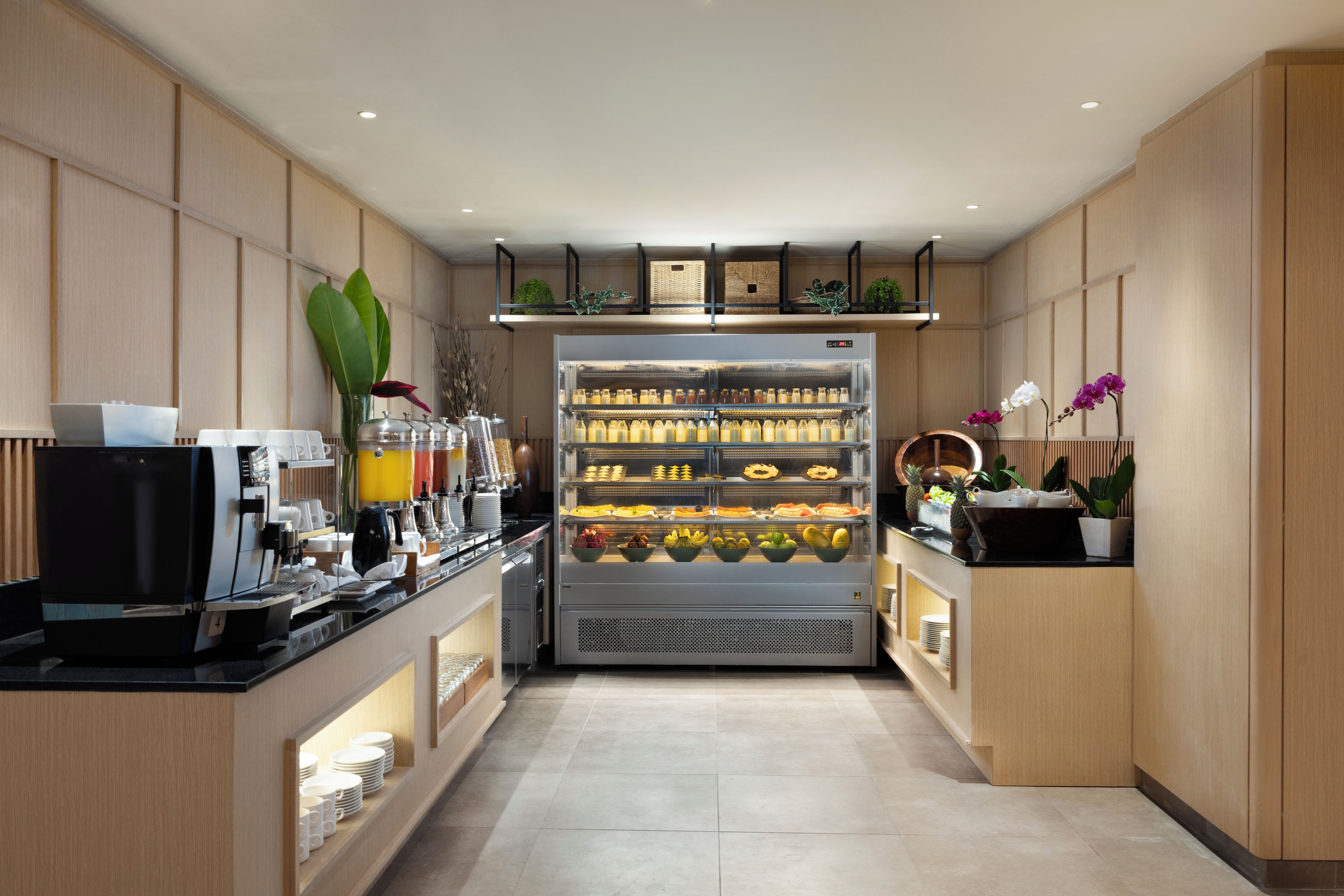 A modern kitchen with a coffee machine, a refrigerated display case with various food items, and a counter with a coffee station.