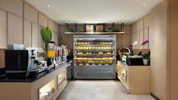 A modern kitchen with a coffee machine, a refrigerated display case with various food items, and a counter with a coffee station.