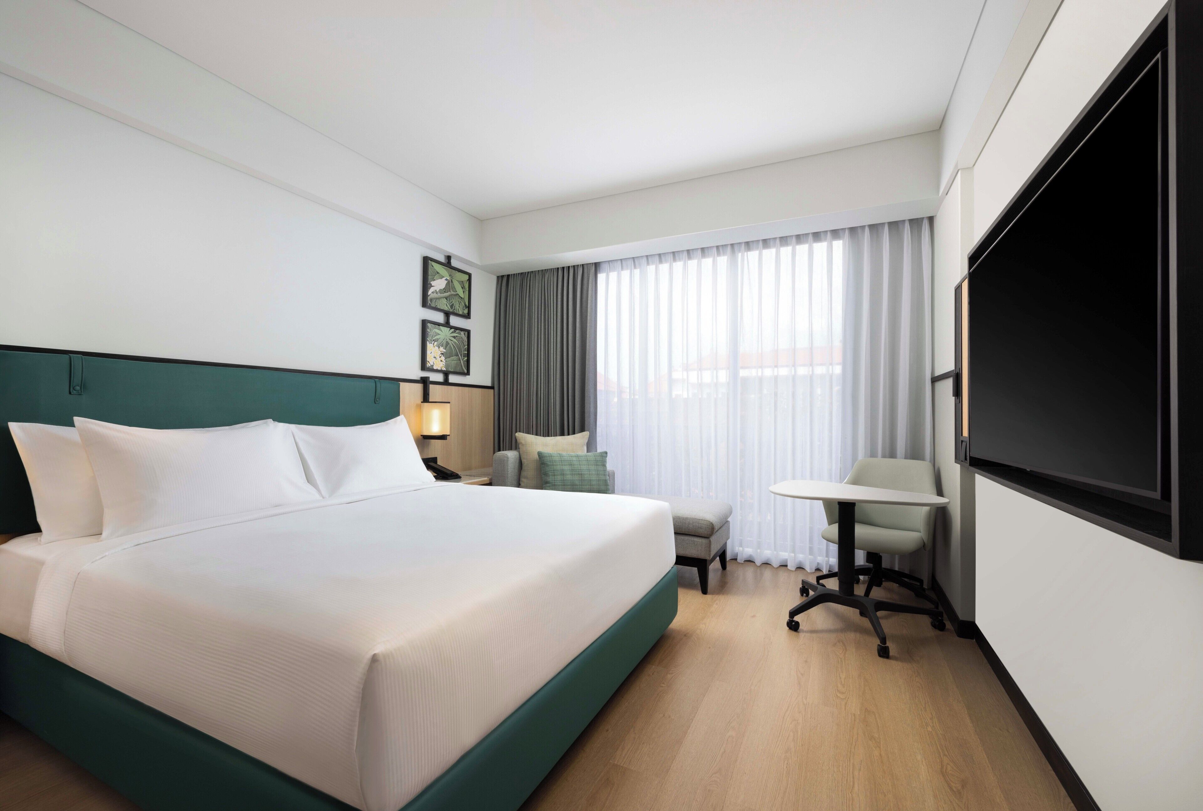 A hotel room with a large bed, a desk, a chair, a TV, and a window with curtains.