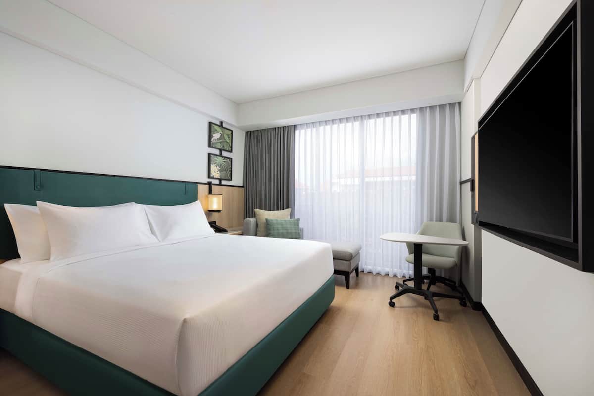 Ein Hotelzimmer mit einem großen Bett, einem Schreibtisch, einem Sessel, einem Fernseher und einem Fenster mit Vorhängen.