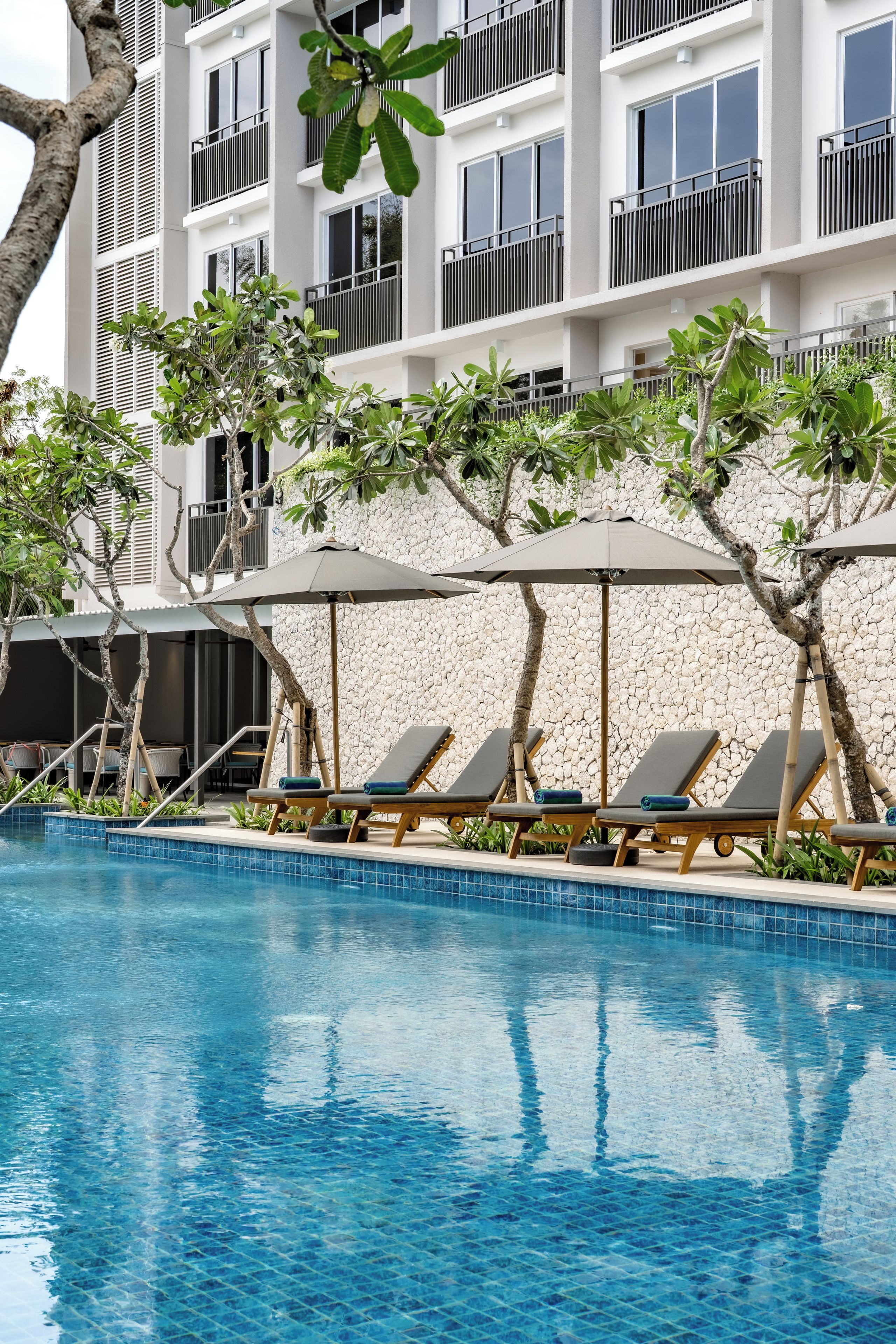 A swimming pool with lounge chairs and umbrellas, surrounded by a stone wall and trees.