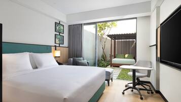 Quarto de hotel moderno com uma cama grande, uma escrivaninha, uma cadeira e uma pequena área de jardim visível pelas portas de correr.