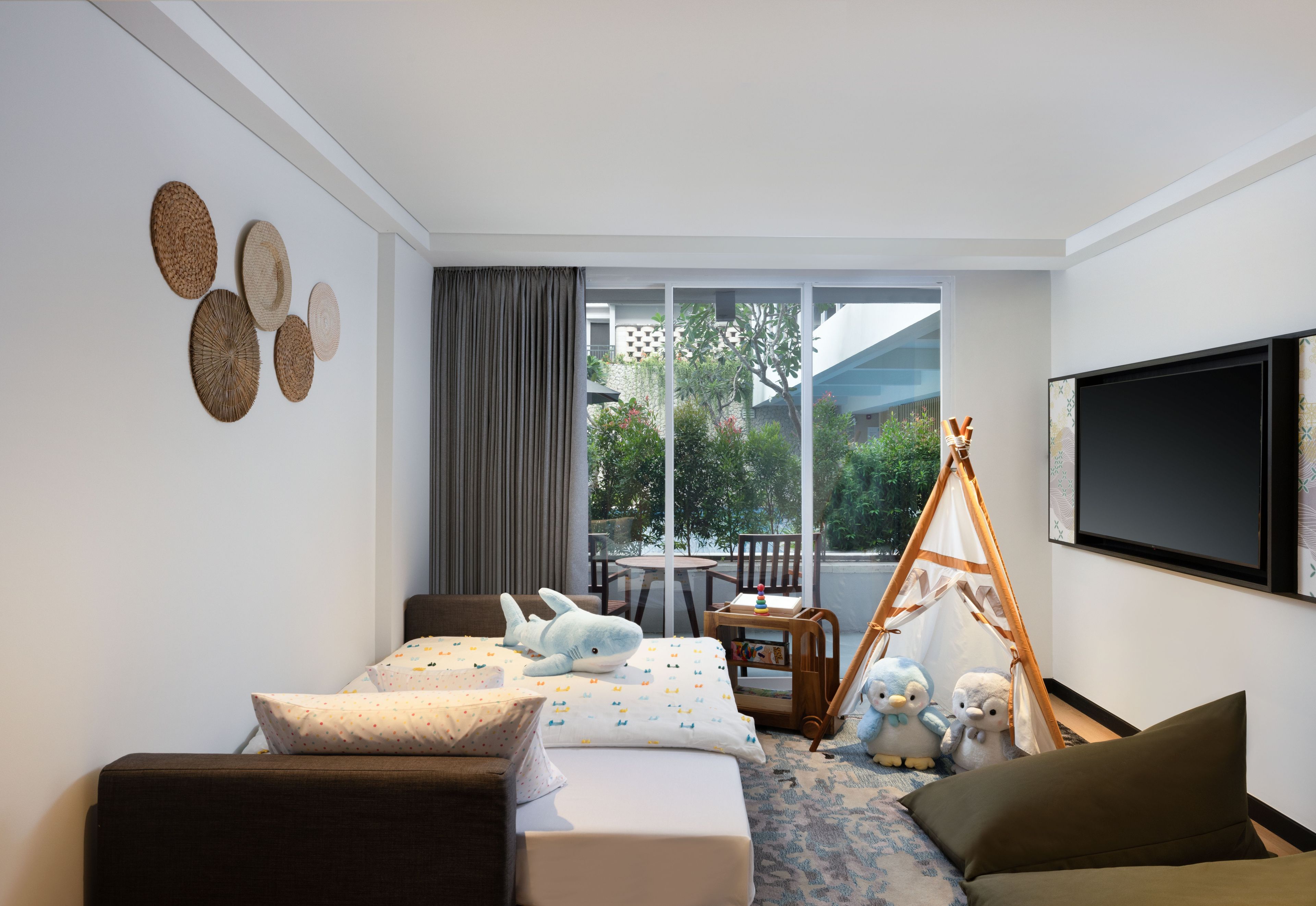 A modern hotel room with a bed, a sofa, a TV, and a balcony with a view of greenery.
