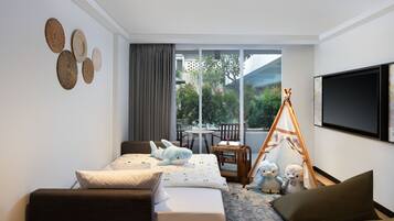 A modern hotel room with a bed, a sofa, a TV, and a balcony with a view of greenery.