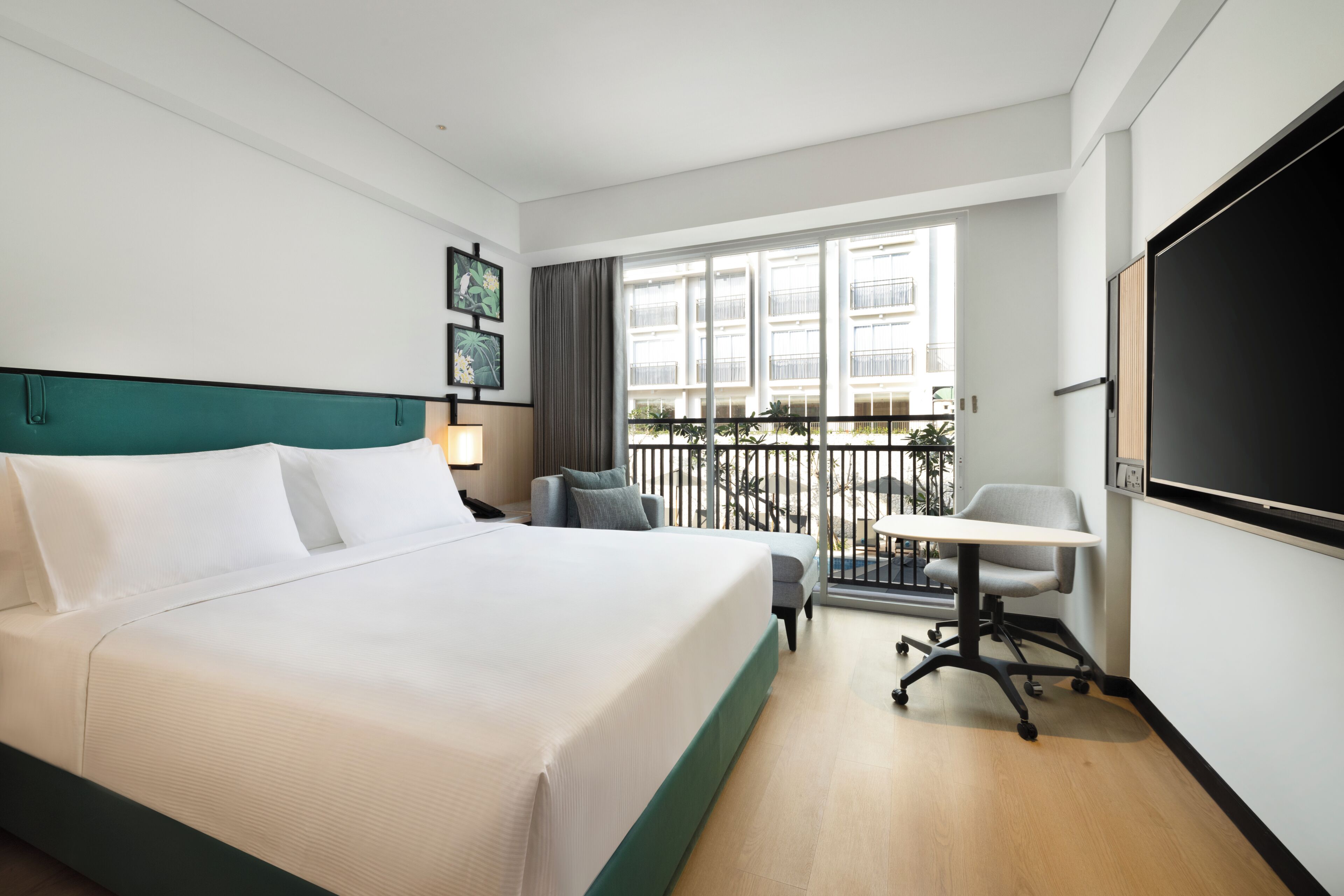 A hotel room with a bed, a desk, a chair, a TV, and a balcony with a railing.
