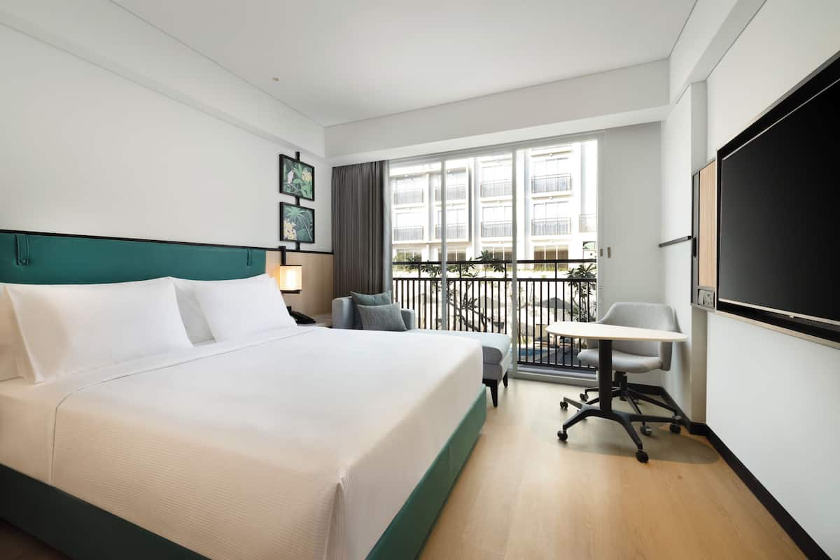 Ein Hotelzimmer mit einem großen Bett, einem Schreibtisch und einem Balkon mit Blick auf Gebäude.