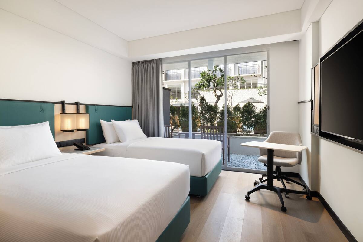 Ein Hotelzimmer mit zwei Betten, einem Schreibtisch, einem Stuhl, einem Fernseher und einem Balkon mit Aussicht.