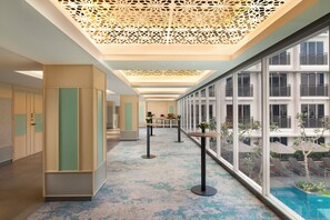 Un couloir d’hôtel moderne avec vue sur la piscine, des panneaux de bois et un plafond décoratif.