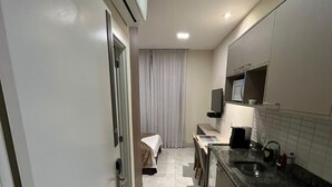 A narrow hallway leading to a bedroom with a bed and a window. A kitchenette with a microwave and sink is visible. - Jacques Pilon Residence (Centro Histórico de São Paulo São Paulo)
