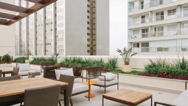 An outdoor patio area with tables and chairs, surrounded by greenery and overlooking a residential building. - Jacques Pilon Residence (Centro Histórico de São Paulo São Paulo)