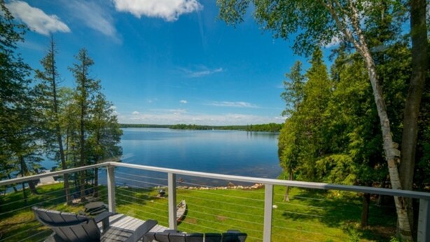 A deck with outdoor furniture overlooking a lake, surrounded by trees.