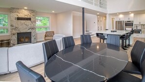 A modern living room with a marble table and black leather chairs, a fireplace, and a kitchen with stainless steel appliances.