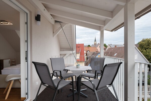 Ein Balkon mit Tisch, Stühlen, einem Bett und Blick auf Gebäude sowie eine Kirche.