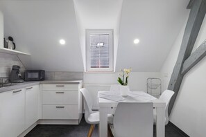 A modern kitchen with white cabinetry, a dining table with chairs, a small window with blinds, and a radiator.