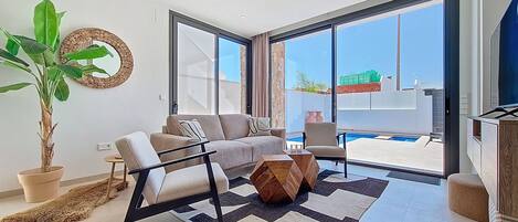 A modern living room with a sofa, armchair, and a large potted plant.