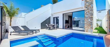 A modern pool area with a clear blue pool, lounge chairs, and a patio with outdoor furniture.