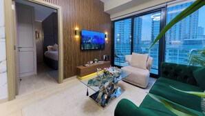 Una sala de estar moderna con un televisor grande, una mesa de centro de vidrio, un sofá verde y vistas de rascacielos.