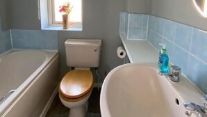 Une salle de bain équipée d’une baignoire, de toilettes, d’un lavabo et d’une fenêtre donnant sur un immeuble.