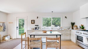 Una cocina luminosa con un gran ventanal, una mesa de comedor con sillas y una estufa.