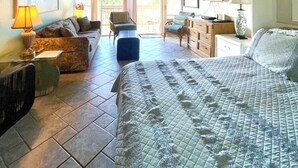A spacious room with a large bed, a sofa, a chair, and a desk. There is a ceiling fan and a window with curtains. - Charming Studio condo in peaceful Kihei with AC, WiFi, pool (Kihei)