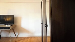 A room with a wooden floor, a television on a stand, and a dark-colored wardrobe.