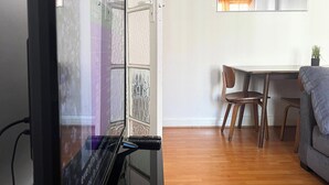 A room with a large flat-screen TV, a dining area with a table and chairs, and a sofa.