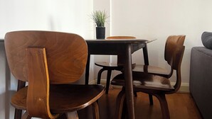 A dining area with a table and four wooden chairs, a small potted plant on the table, and a grey sofa in the background.