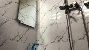 Een badkamer met wandtegels in marmerlook, een handdouche, een wastafel met een blauwe kraan en een handdoek aan de muur.