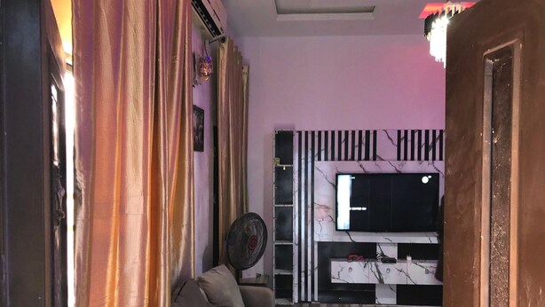 Een woonkamer met een bank, een aan de muur bevestigde televisie, een ventilator en gordijnen.