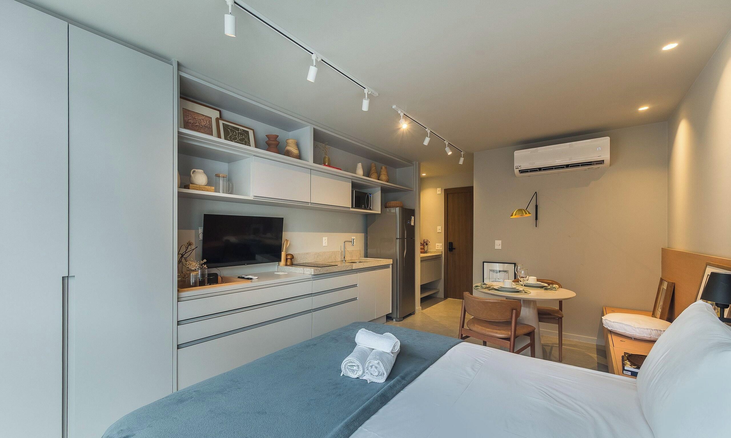 A hotel room with a bed, a desk, a chair, a television, and a kitchenette.