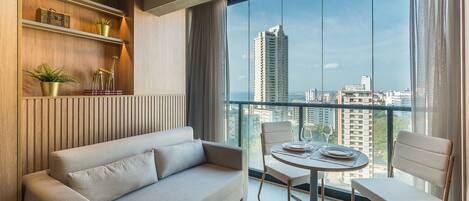 A modern living room with a sofa, chairs, a small table, and a view of the city through large windows.