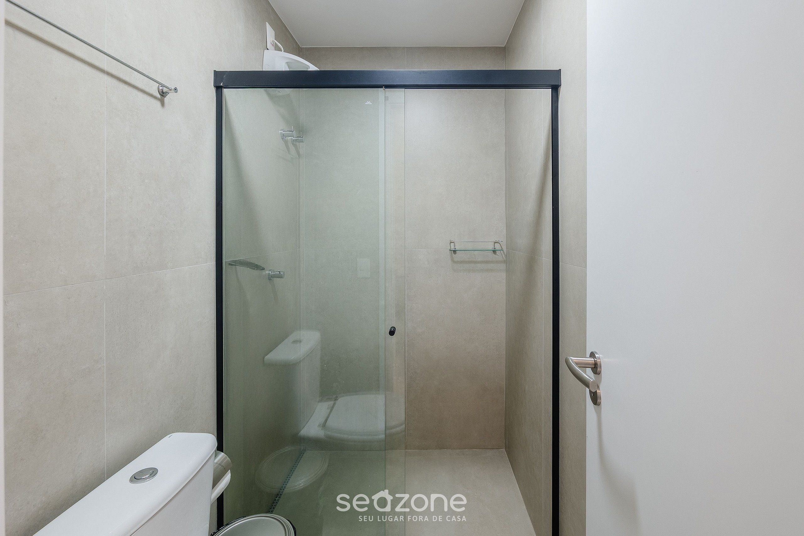 A glass-enclosed shower stall with a toilet and a towel rack.