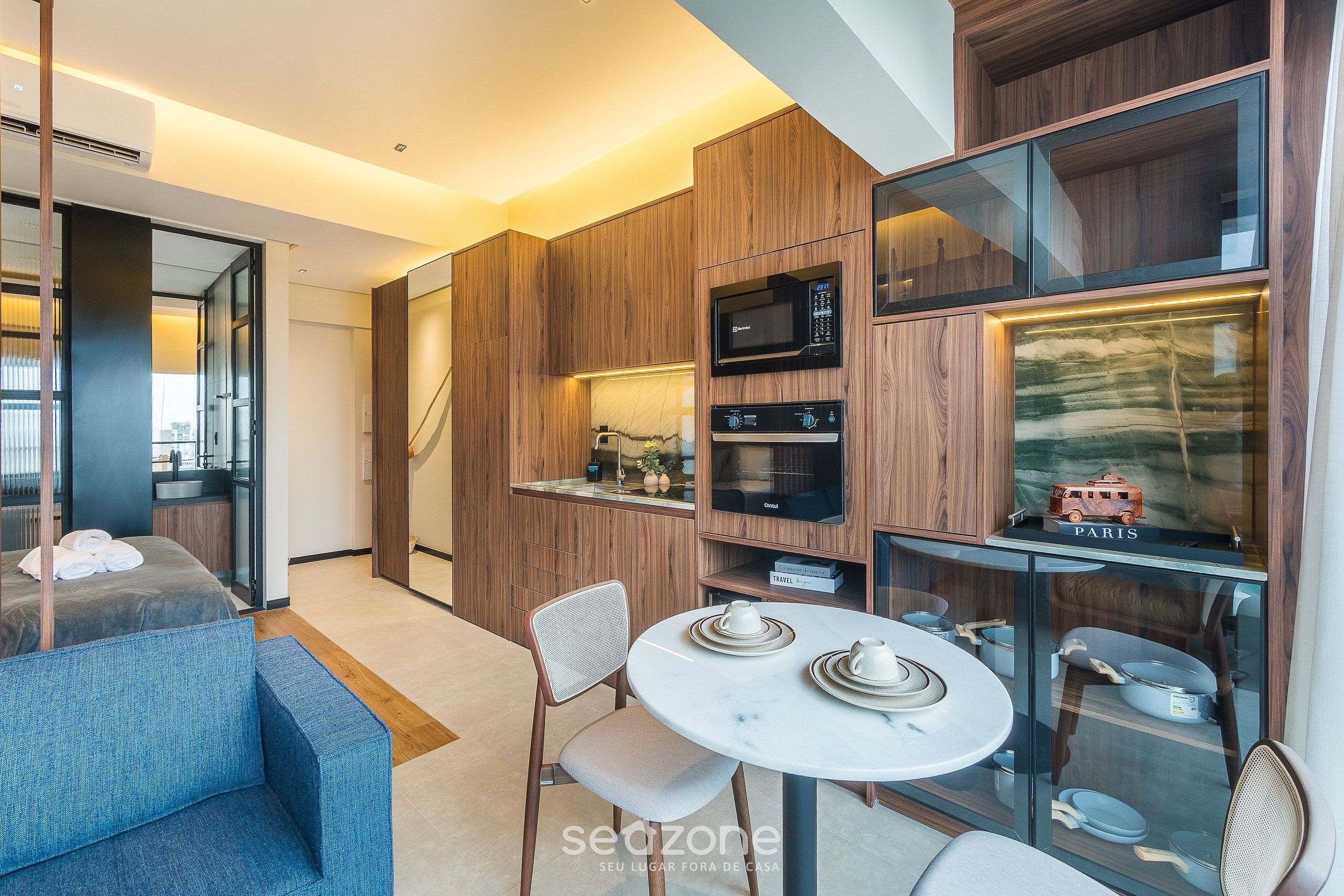 A modern kitchen with wooden cabinets, a microwave, and a glass display case with kitchenware.