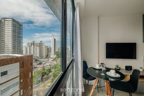 A modern room with a large window, a flat-screen TV, a dining table with chairs, and a small plant. - Stay With Style and Convenience in Salvador LIV (Salvador)