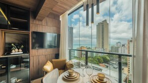 A modern living room with a large TV, a dining table with plates and glasses, and a view of the cityscape through large windows. - Stay With Style and Convenience in Salvador LIV (Salvador)