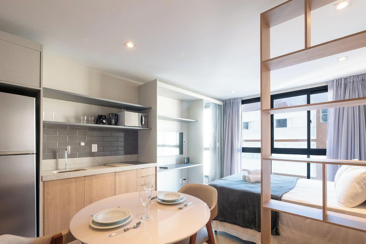 A compact hotel room with a kitchenette, a dining area, and a bed with a view.