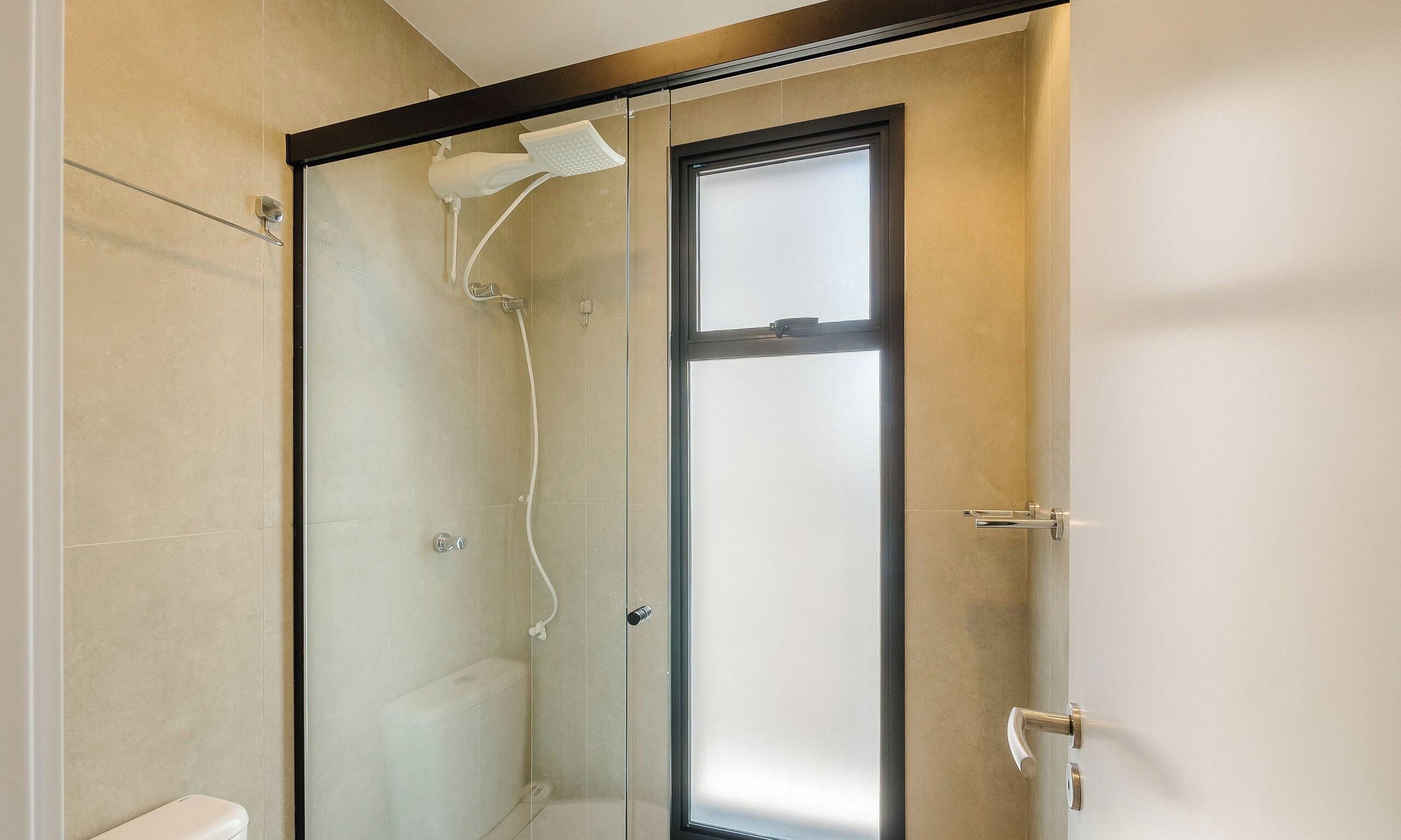 A glass-enclosed shower with a handheld showerhead and a door with a handle.