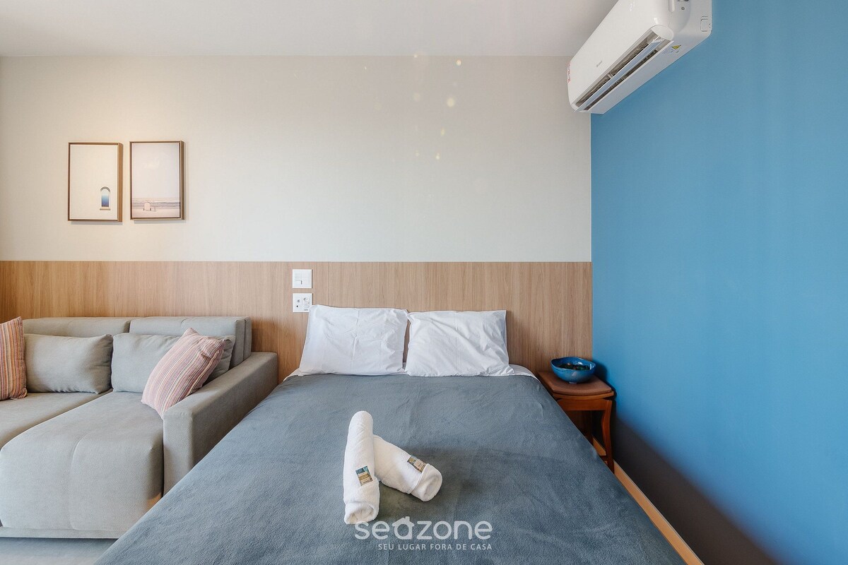 Habitación de hotel con cama, sofá, una mesita con un tazón y dos cuadros en la pared.