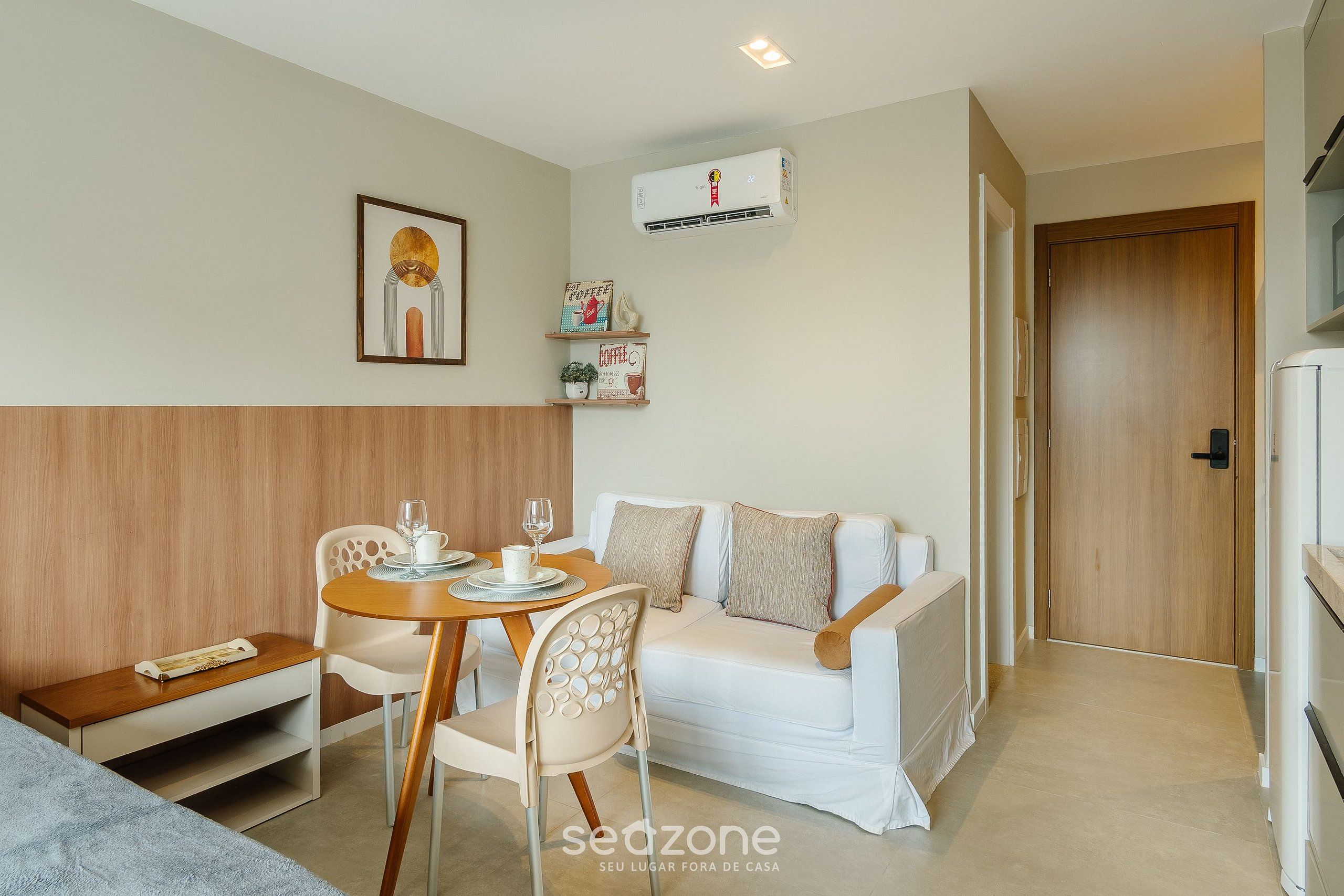 Une pièce moderne avec un canapé blanc, une table à manger en bois avec des chaises, un petit meuble blanc et un climatiseur fixé au mur.