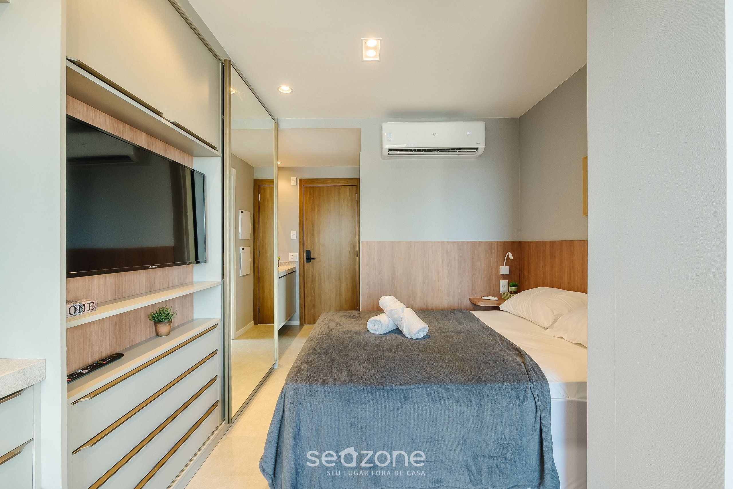 A modern hotel room with a bed, a TV, a wardrobe, and an air conditioning unit.