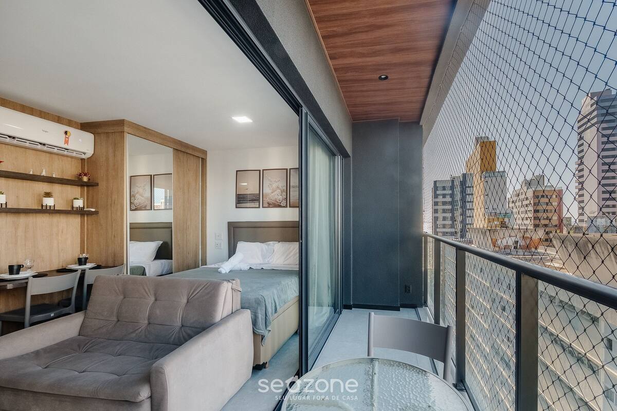 A modern hotel room with a balcony, a bed, a sofa, and a dining area.