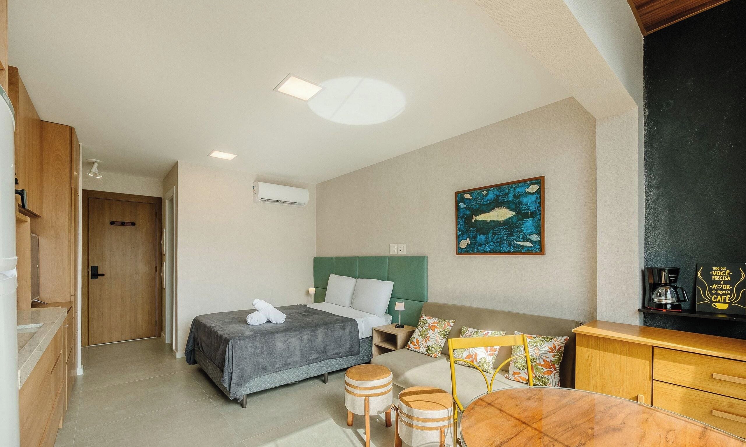 A hotel room with a bed, a desk, a chair, a coffee machine, and a painting on the wall.