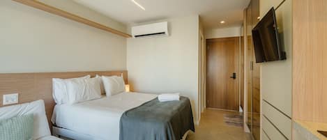 A hotel room with a bed, a sofa, an air conditioning unit, a television, and a wooden wardrobe.