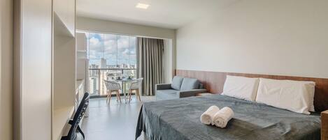 Ein Hotelzimmer mit einem Bett, einem Sofa, einem Esstisch mit Stühlen und einem Balkon mit Stadtblick.