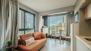 A modern living room with a sofa, a dining table with chairs, a small side table, and a view of tall buildings through large windows. - Stay With Style and Convenience in Salvador LIV (Salvador)
