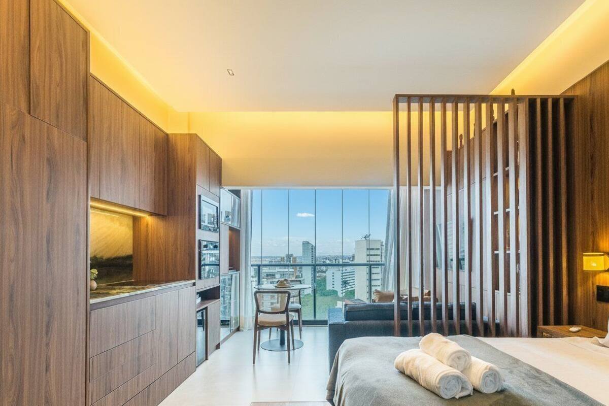 A modern hotel room with a large bed, a desk, and a view of the city.