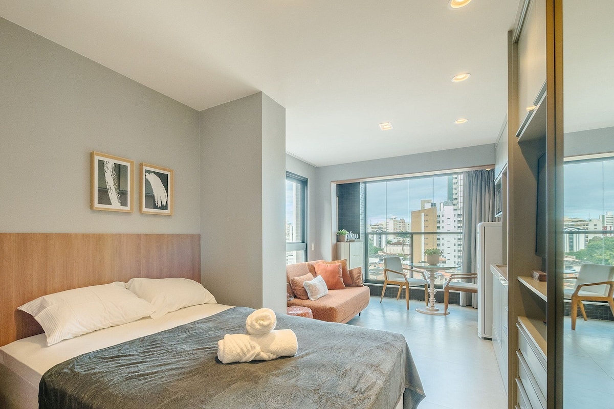A hotel room with a bed, a seating area with a table and chairs, and a large window offering a city view.
