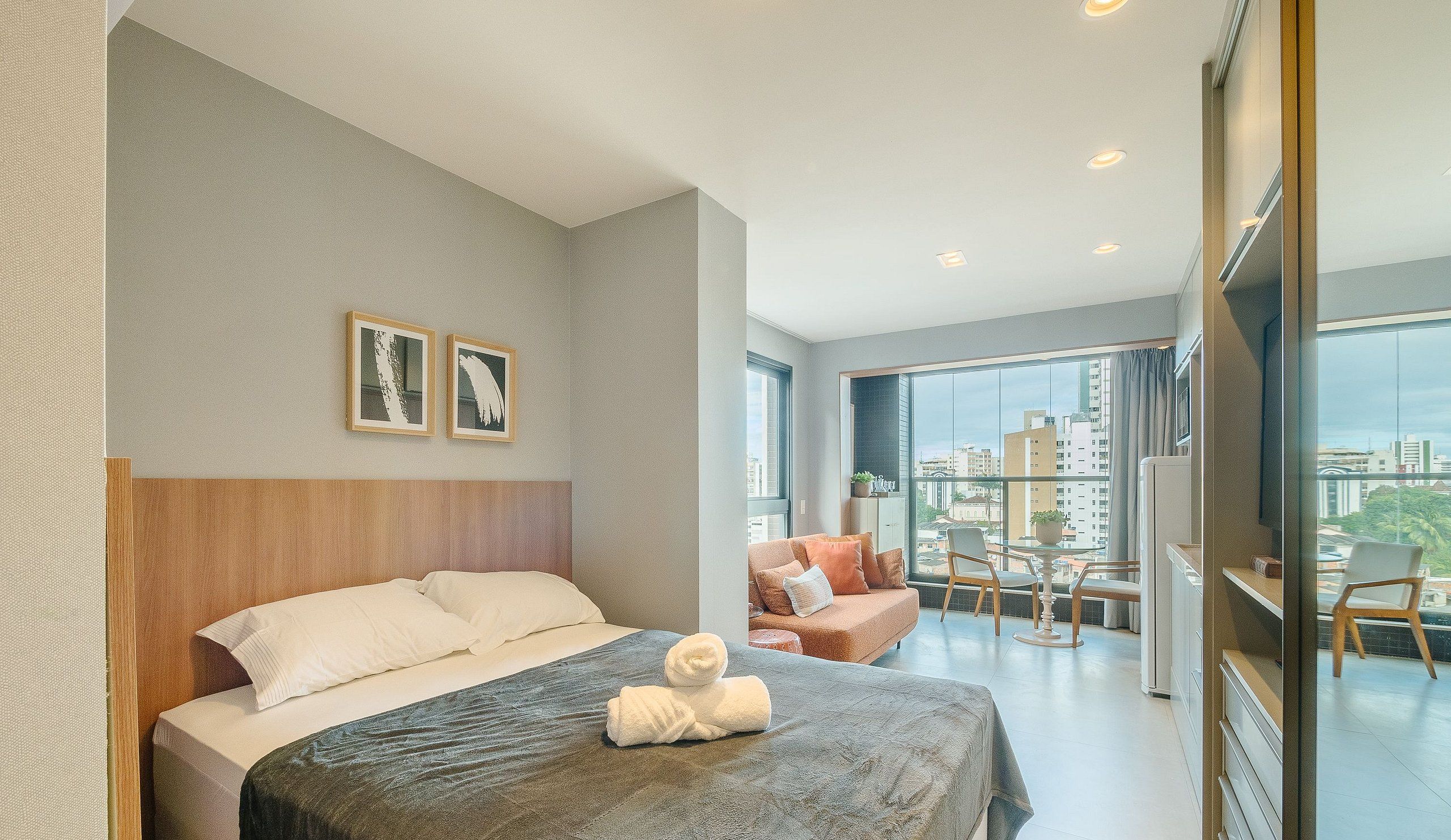 Habitación de hotel con cama, zona de estar con mesa y sillas, y un gran ventanal con vistas a la ciudad.