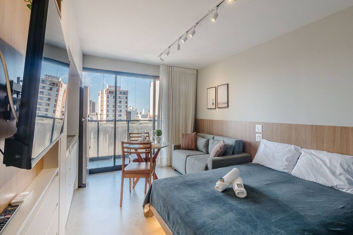 A hotel room with a balcony, a bed, a sofa, and a dining area.