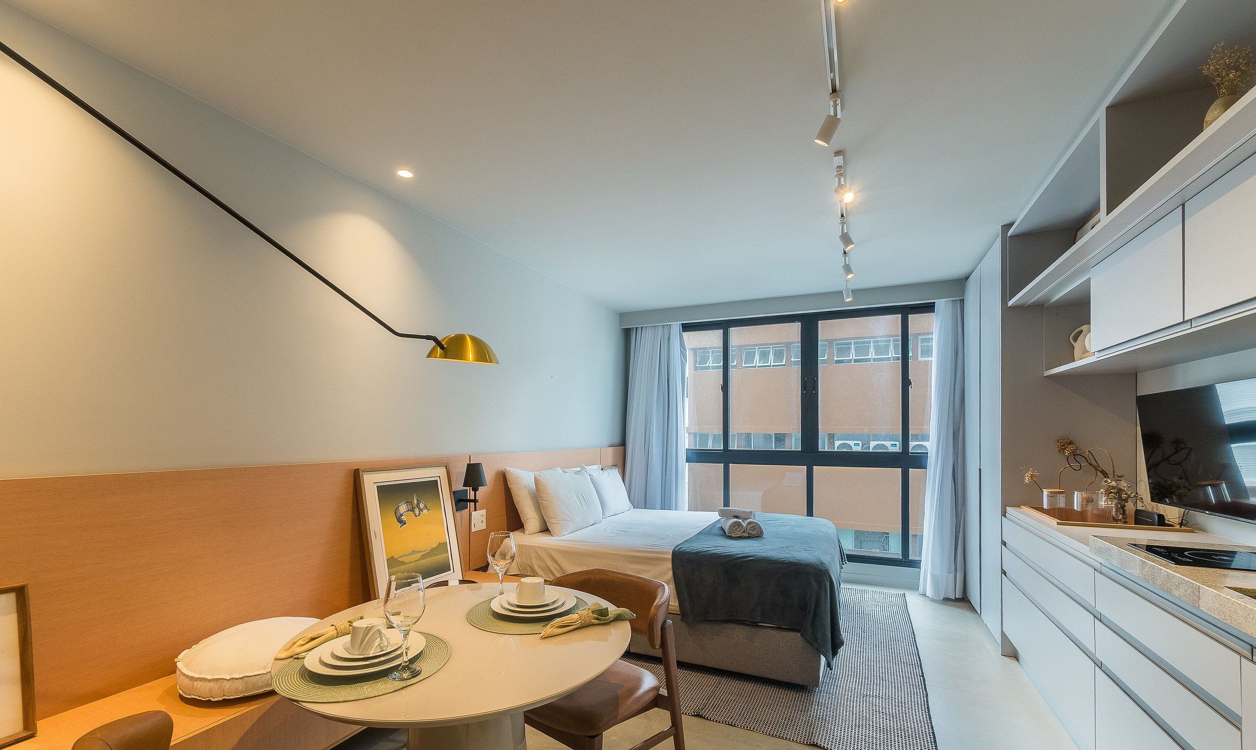 Una habitación de hotel compacta con cama, una mesa de comedor con una silla, una pequeña cocina y un amplio ventanal con vistas al exterior.
